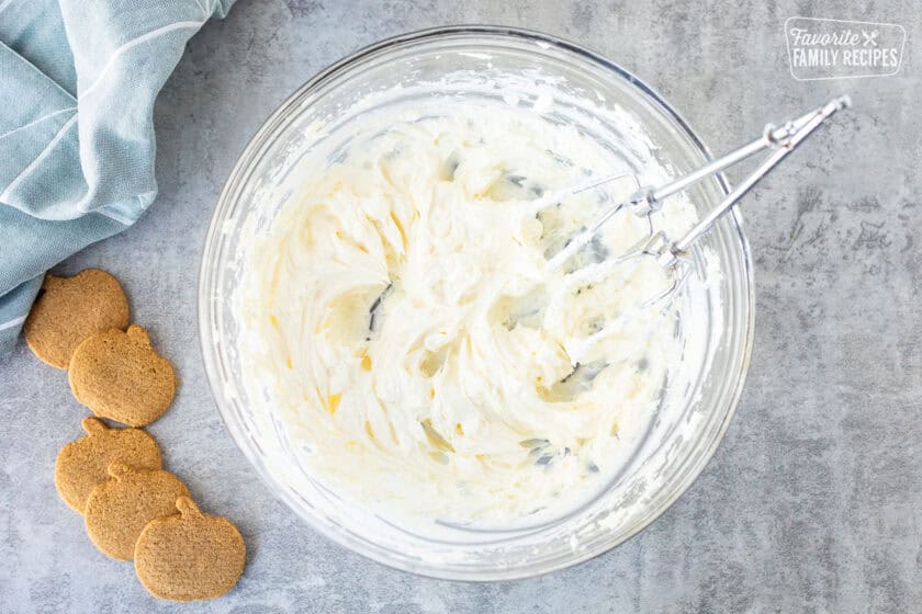 Glass mixing bowl with whipped cream cheese and electric beaters.