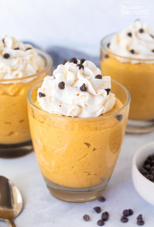 Pumpkin mousse in glass dessert cups topped with whipped cream, mini chocolate chips, and a dusting of spice.