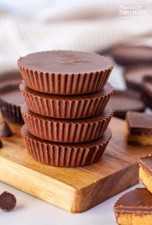 Reese’s peanut butter cups stacked on a wooden board, with cut pieces showing the peanut butter filling and chocolate shell.