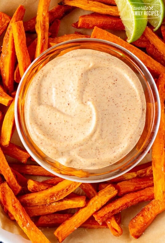 Creamy sweet potato fries dipping sauce in a glass bowl surrounded by golden sweet potato fries and lime wedges.